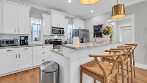 A modern kitchen with white cabinetry, stainless steel appliances, a central island with bar stools, and pendant lighting. - 🦩Book Me Baby! Ain't Life Grand 30A~GolfCart~6bikes🦩 (Santa Rosa Beach)
