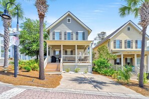 A two-story house with a front porch, a stop sign, and a palm tree.