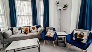 Ein modernes Wohnzimmer mit einem grauen Sofa, blauen Sesseln und einem weißen Couchtisch.