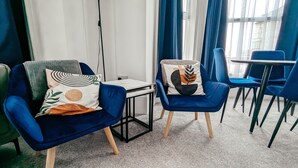 Ein modernes Zimmer mit zwei blauen Sesseln, einem kleinen Tisch und Blick durch große Fenster.