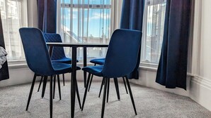 Ein Essbereich mit zwei blauen Stühlen und einem Tisch neben einem Fenster mit Vorhängen.