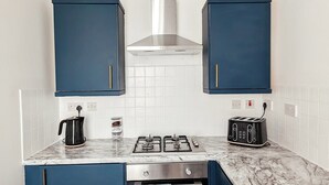 A kitchen with blue cabinets, a gas stove, a kettle, and a toaster. - Ocean View Apartment (Bridlington)