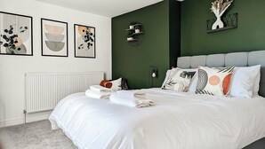 A neatly made bed with white linens and multiple pillows, a green accent wall, and framed artwork on the wall. - Ocean View Apartment (Bridlington)