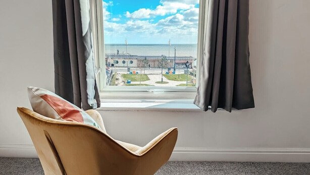 Habitación con vista a un edificio y al mar, a través de una ventana con cortinas.