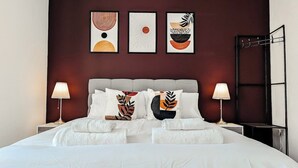 Una cama bien hecha con sábanas blancas, dos lámparas de noche y tres cuadros en la pared.