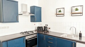Una cocina con armarios azules, estufa a gas, lavamanos y cafetera.