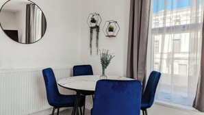 Comedor con una mesa redonda, cuatro sillas azules, una mesa de mármol blanco y dos jardineras hexagonales fijadas a la pared con plantas colgantes.