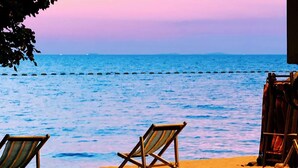 A beach scene with two lounge chairs facing the sea, a wooden fence, and a clear view of the ocean. - The EDGE (Pattaya)