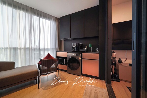 Una sala de estar moderna con un sofá, una silla, una lavadora y una zona de cocina con armarios y electrodomésticos.