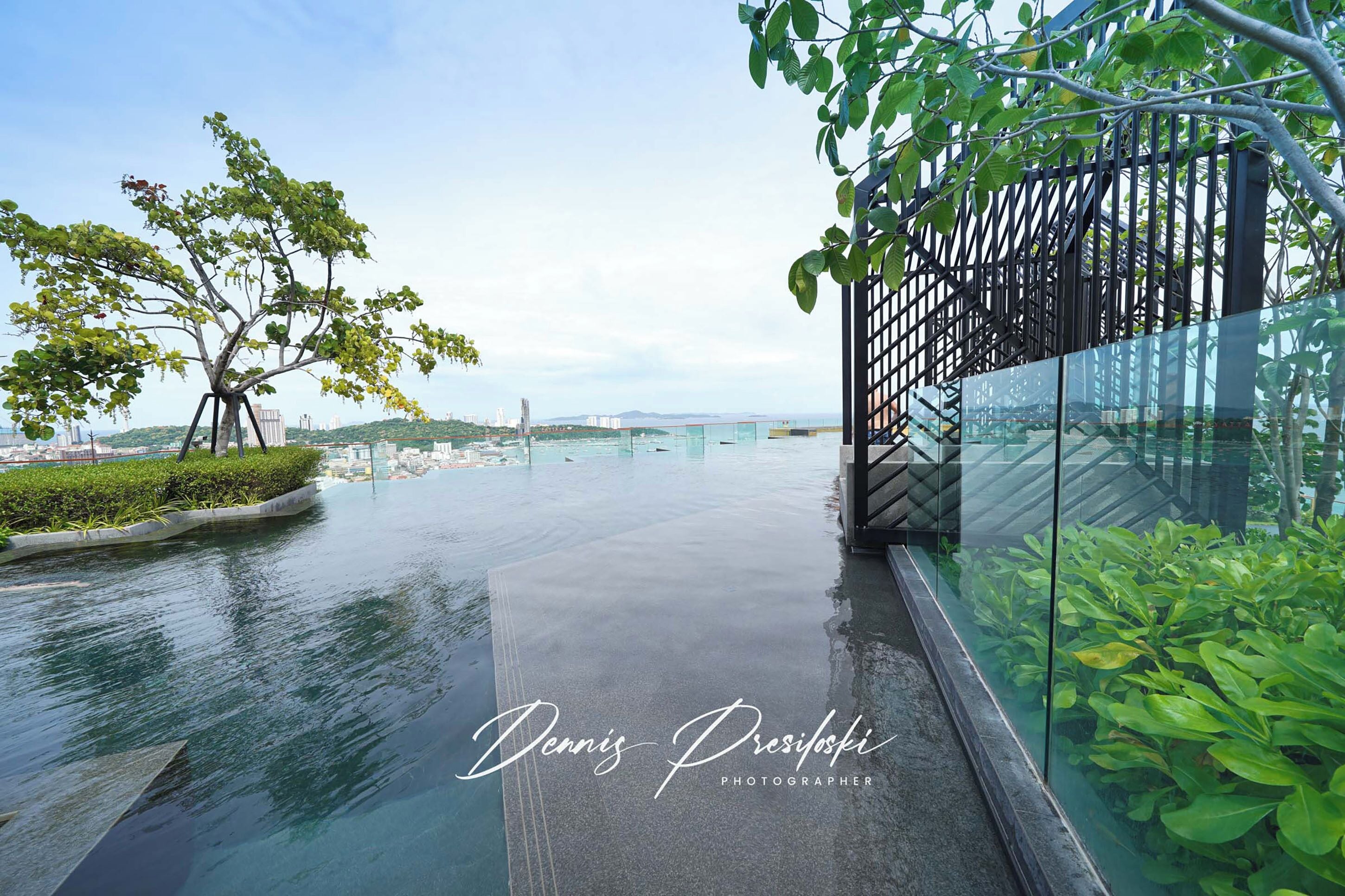 A modern outdoor area with a glass railing, a tree, and a view of a bridge in the distance.