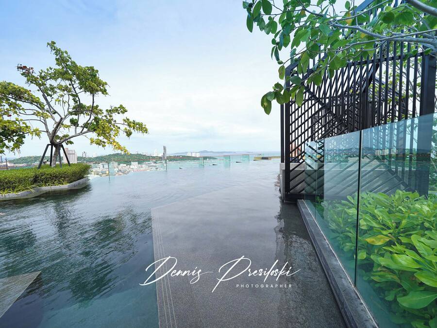 A modern outdoor area with a glass railing, a tree, and a view of a bridge in the distance.