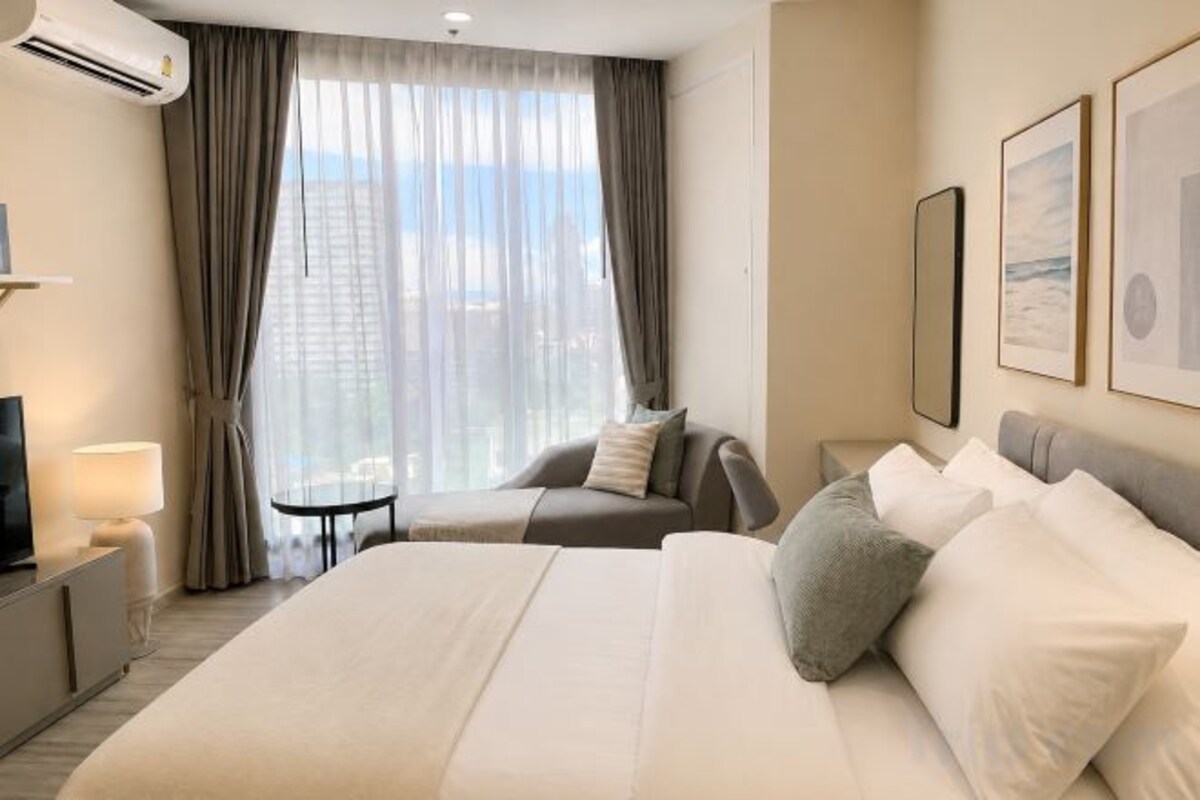Quarto de hotel com uma cama grande, sofá, televisão e janela com cortinas.