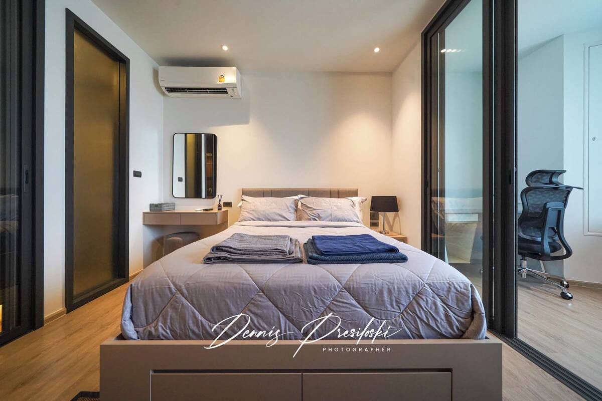 A modern bedroom with a large bed, a bedside table, a mirror, and a chair.