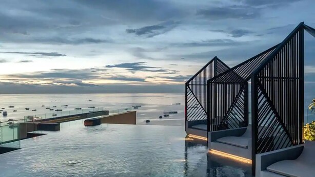 An infinity pool with a view of the sea and boats, a modern architectural structure with geometric lines, and a glass barrier separating the pool from the water. - The EDGE (Pattaya)