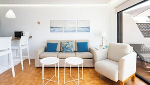 Een moderne woonkamer met een bank, twee witte bijzettafeltjes, een witte stoel en een glazen tafel.