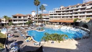 Een resort met een groot zwembad, omringd door ligbedden en palmbomen.