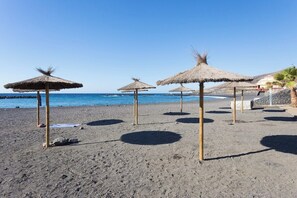 A beach with thatched umbrellas and a clear blue sky.