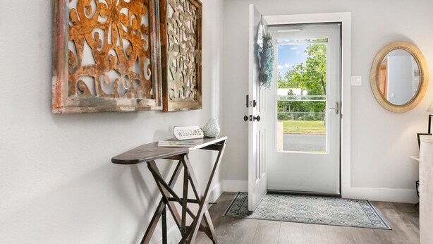 Un pasillo con una puerta blanca, un cartel de bienvenida, una pequeña mesa con un florero y dos paneles decorativos en la pared.