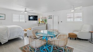 A modern, well-lit room with a glass-top table surrounded by wicker chairs, a white sofa, and a white armchair. - The Historic Coquina Cottages C is 2 Blocks to the Beach, 5th Avenue and 3rd St. (Naples)