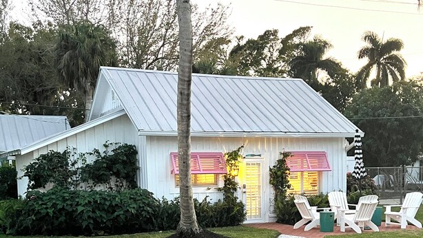 A white house with a metal roof, surrounded by a well-maintained lawn and a gravel path leading to a seating area with white chairs. - The Historic Coquina Cottages C is 2 Blocks to the Beach, 5th Avenue and 3rd St. (Naples)