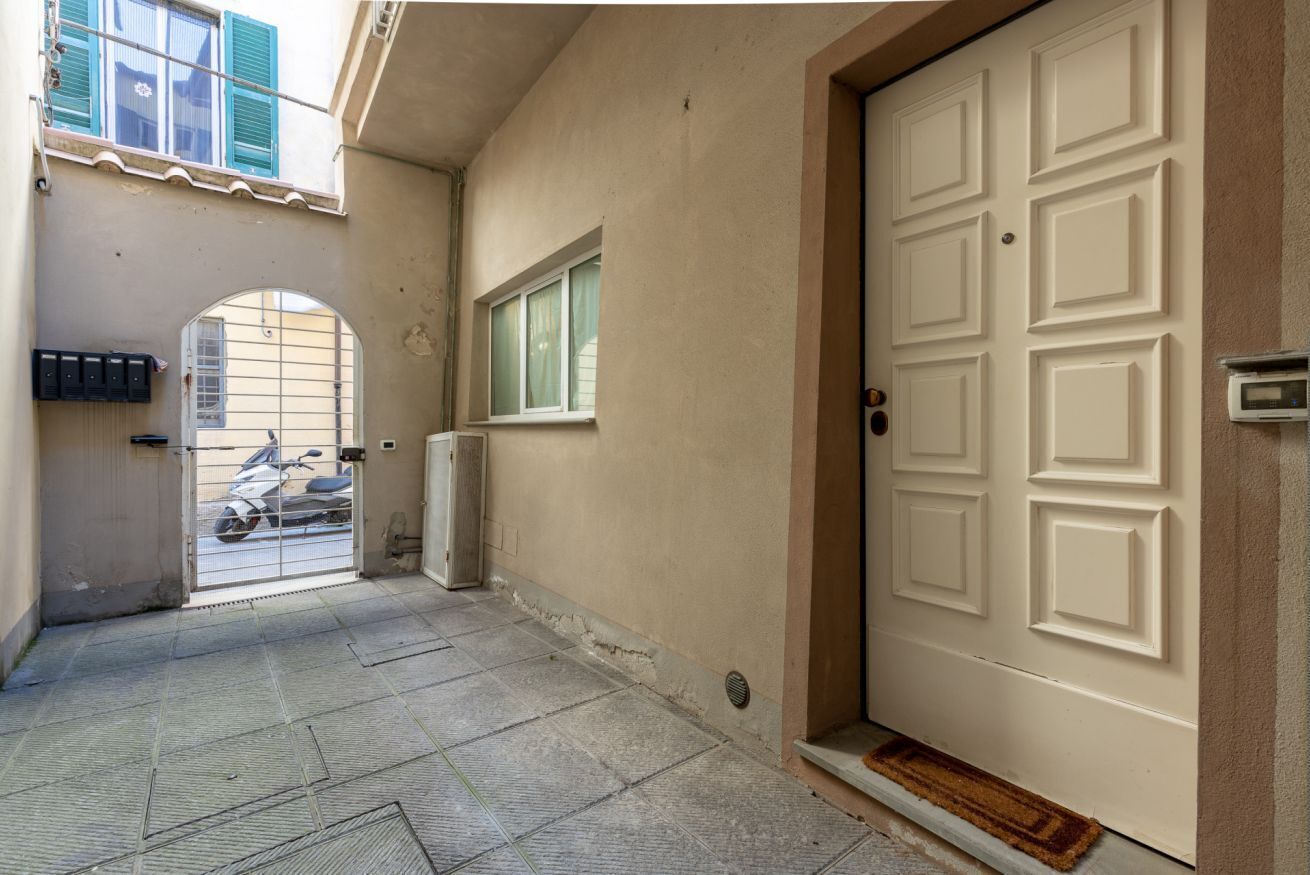 A narrow hallway with a white door, a window with a curtain, and a scooter parked outside.