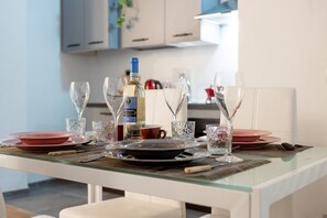Une table à manger dressée avec des assiettes, des verres et une bouteille, avec une cuisine en arrière-plan.
