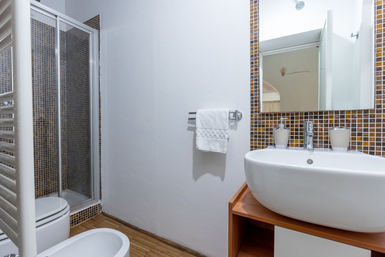 Une salle de bain avec un lavabo blanc, deux tasses, une serviette, une douche et des toilettes.