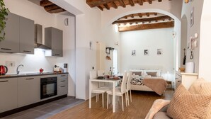 Una cocina moderna con armarios blancos, un comedor con mesa y sillas, y un dormitorio con cama y ventana.