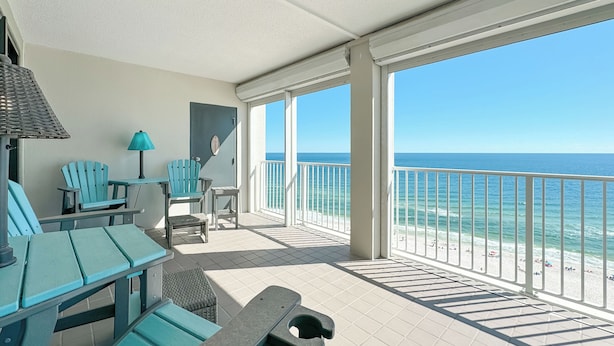 Un balcon avec vue sur l’océan, des chaises turquoise, une table et une lampe.