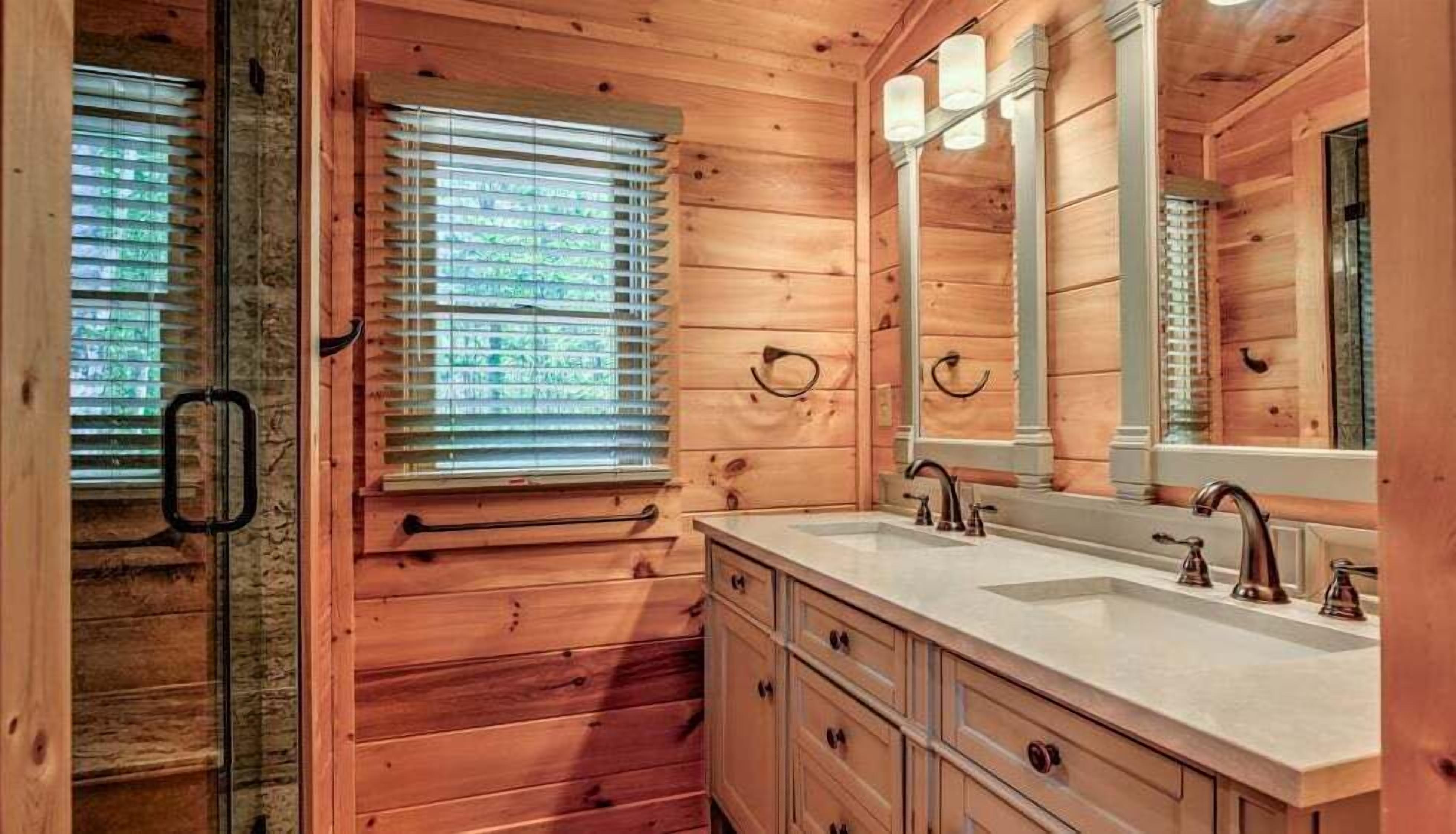 Une salle de bain rustique, avec une cabine en bois, un meuble-lavabo à deux vasques, des armoires en bois et un grand miroir.