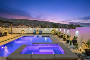 A swimming pool with a view of mountains at dusk, surrounded by potted plants and a patio area with seating. - New: Spacious Backyard, Pool & Hot Tub, Gameroom (Desert Hot Springs)