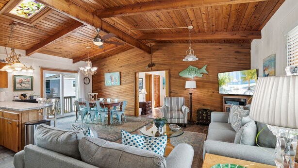 A spacious living area with a wooden ceiling, a dining table with chairs, a sofa, and a television.