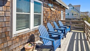 A wooden deck with blue Adirondack chairs and a potted plant.