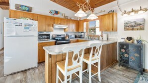 A modern kitchen with wooden cabinets, a central island with bar stools, stainless steel appliances, and a hanging light fixture.