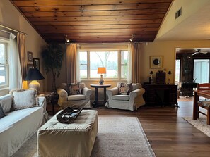 Ein gemütliches Wohnzimmer mit Holzbalkendecke, zwei Sesseln, einem Sofa, einem Couchtisch und einem Essbereich mit einem Holztisch und Stühlen.