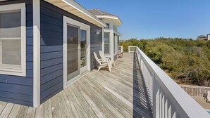 A wooden deck with a railing, a sliding glass door, and two white chairs. - Despacito: Pool, Hot Tub, Walk to Beach OBX (Corolla)