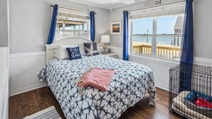 Un dormitorio con cama, ventilador de techo, ventana con vista a la playa y una pequeña cama para perro.