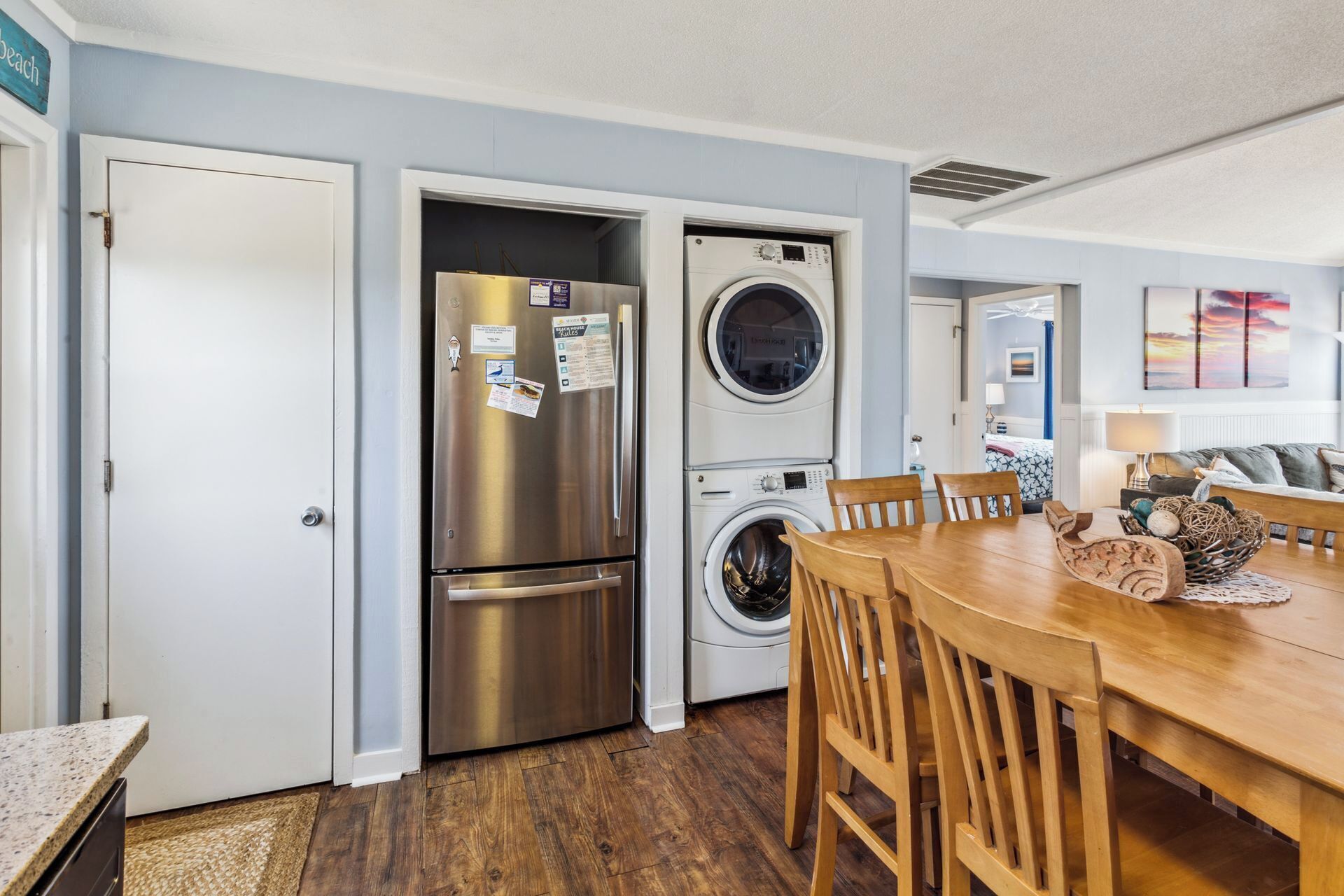 A compact kitchen with a stainless steel refrigerator, a built-in washer and dryer, and a wooden dining table with chairs.