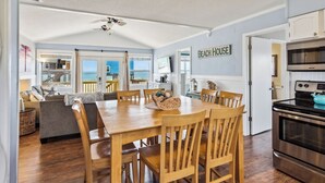 Un rincón comedor acogedor con una mesa y sillas de madera, una cocina con estufa y microondas, y vista al océano a través de grandes ventanales.