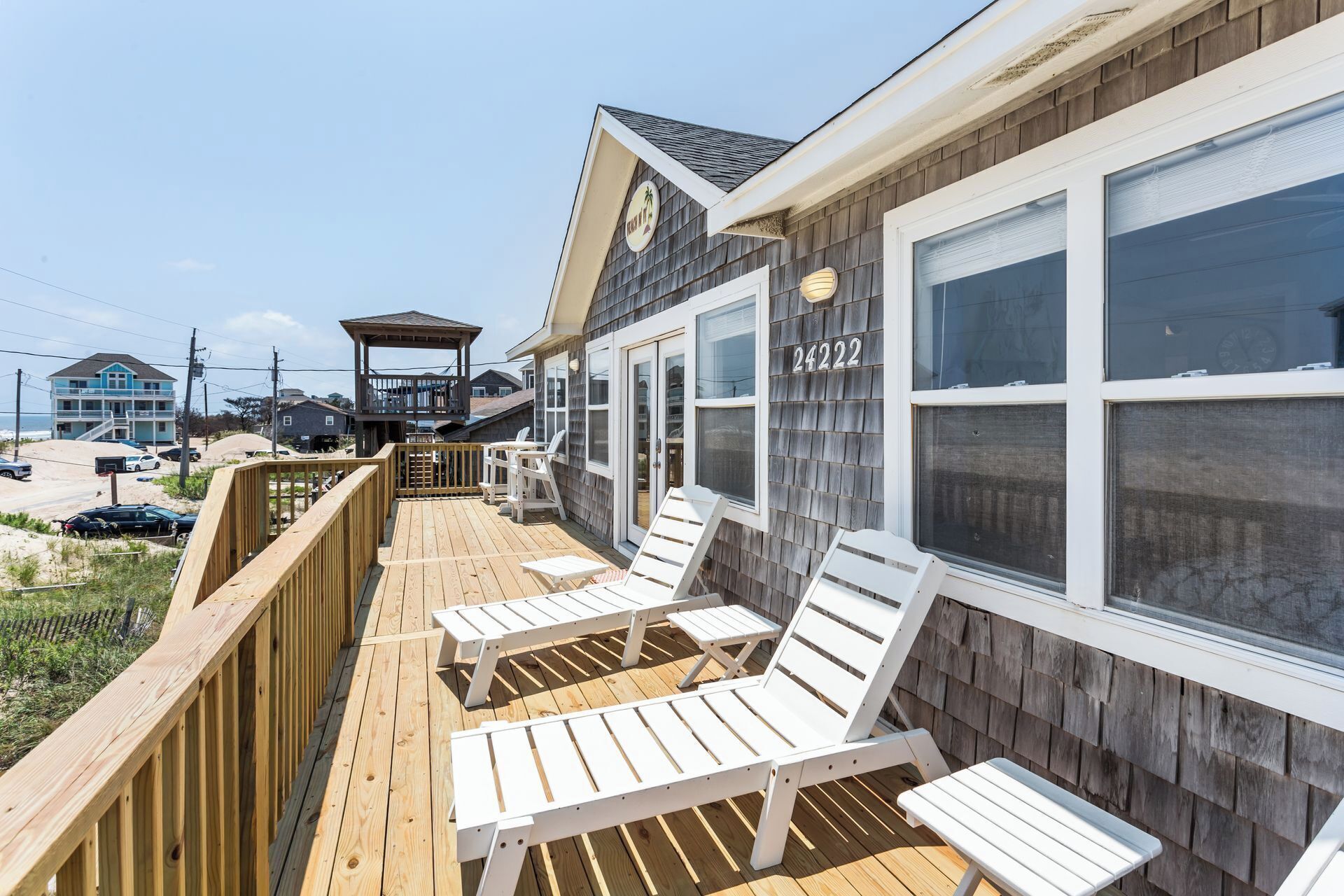 A wooden deck with white lounge chairs, a covered area with a gazebo, and a large window with the number 24222.