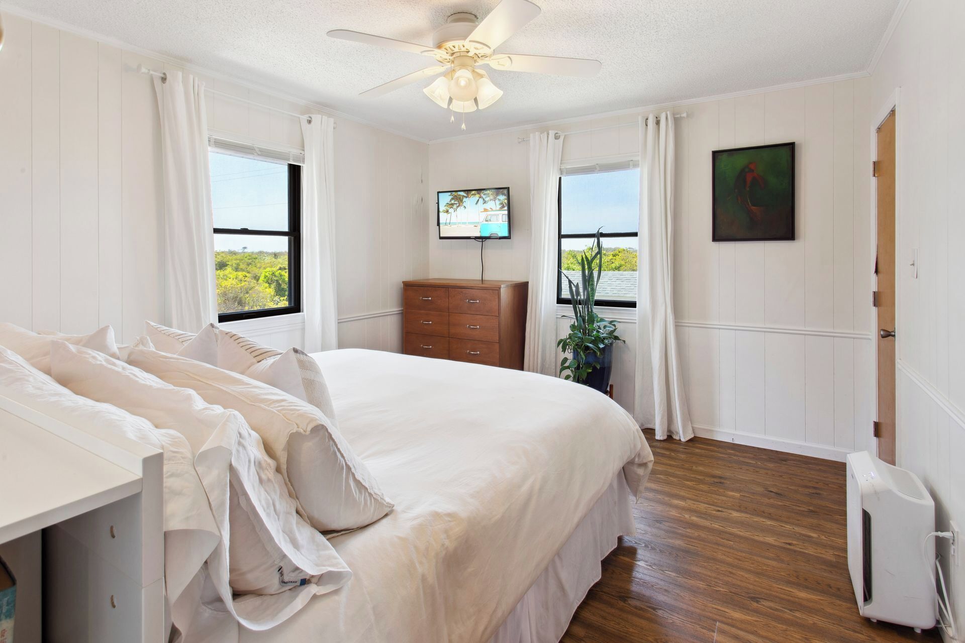 Une chambre à coucher avec un lit, une commode, un téléviseur et une fenêtre donnant sur un beau paysage.