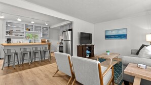 A modern kitchen with bar stools, a dining table, and a gray sofa in a bright living area with a view of the ocean. - Cozy Home Near Downtown | Newly Added Amenities! | Labor Day Open! (Cedar)