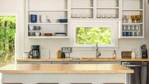 A modern kitchen with a central island, bar stools, and a window overlooking greenery. - Cozy Home Near Downtown | Newly Added Amenities! | Labor Day Open! (Cedar)