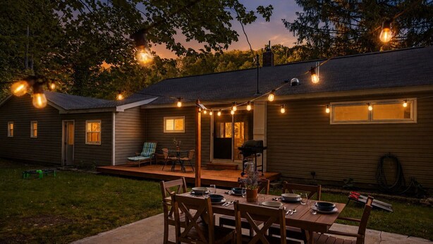 A backyard with a wooden deck, a dining table set for four, and string lights. - Cozy Home Near Downtown | Newly Added Amenities! | Labor Day Open! (Cedar)