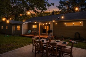 A backyard with a wooden deck, a dining table set for four, and string lights.