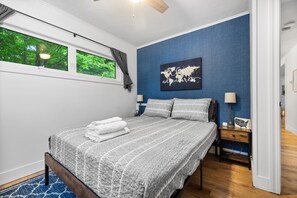A bedroom with a bed, a nightstand, a lamp, a world map artwork, and a window with a view of trees. - Cozy Home Near Downtown | Newly Added Amenities! | (Cedar)