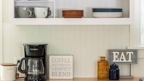 A kitchen with white shelves holding various bowls and cups, a coffee maker, and a sign that says "COFFEE AND FRIENDS A PERFECT BLEND". - Cozy Home Near Downtown | Newly Added Amenities! | Labor Day Open! (Cedar)