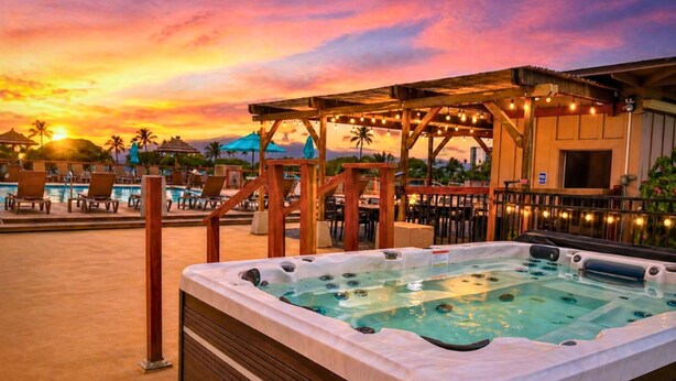 Een hottub met een houten terras, lounge stoelen en parasols.
