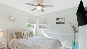 A bedroom with a bed, a ceiling fan, a window, and a vase with flowers.