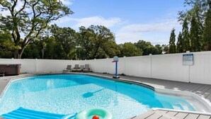 A swimming pool with a wooden deck, lounge chairs, and a sign indicating pool rules.